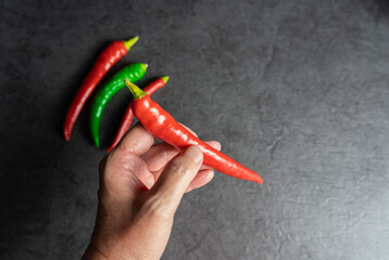 Woman holds a red chili pepper in her hand, in the black background are still red and green chili...