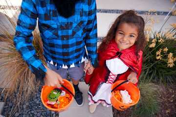 Portrait Of Two Children Wearing Fancy Dress Outside House Collecting Candy For Trick Or Treat