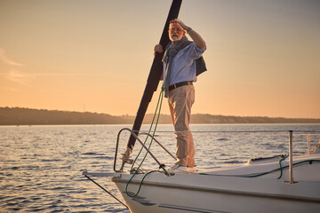 Sailing man on yacht. Elegant senior man standing on the side of a sailboat or yacht deck floating...