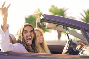 Happy young couple having fun inside convertible sport car. Couple listening to rock music....