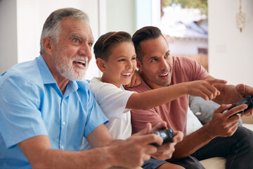 Obraz premium Multi-Generation Male Hispanic Family Playing Video Game At Home Sitting On Sofa Together