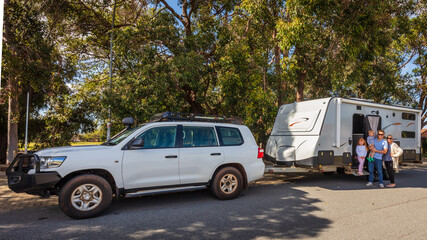 A Young Family proudly standing outside of their  caravan  and 4WD in front of a Park