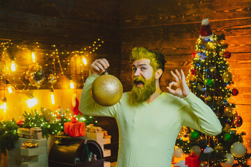 Portrait of handsome Santa indoors with Christmas ball, gold bauble. Happy Santa dressed in winter clothing think about Christmas near Christmas tree. Theme Christmas holidays and winter new year.