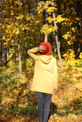 Young woman/female in yellow coat and orange hat walking in a colorful fall/autumn forest or woods. Lifestyle inspirational image with copy space for message. Lifestyle season. 