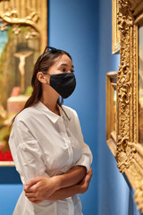 Woman visitor wearing an antivirus mask in the historical museum looking at pictures.