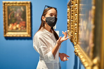 Woman visitor wearing an antivirus mask in the historical museum looking at pictures.