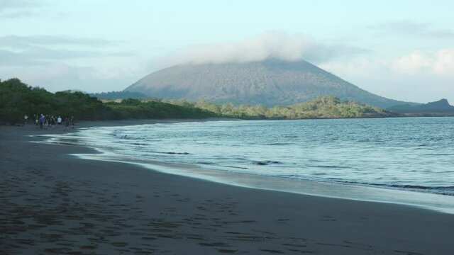 Tourists Walking on Espumilla Beach in Front of Volcanic Hill with Breaking Waves on Santiago Island, Galapagos