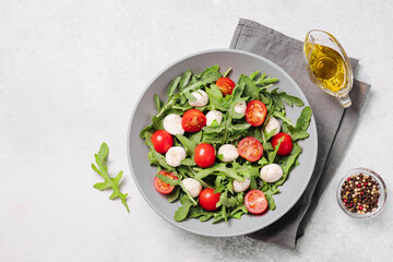 Diet and healthy salad with arugula, cherry tomatoes, mozzarella cheese and olive oil on white background