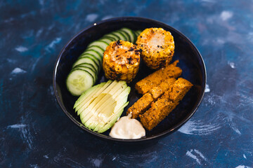 vegan nourish bowl with avocado cucumber polenta chips and spicy corn on the cob with vegan mayo