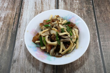 Traditional fried and stirred fresh mushroom with chopped pork belly and sliced spring onion seasoning with soy sauce and pepper on the plate. Famous pork and mushroom menu in Asia restaurant. 
