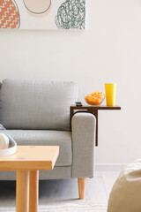 Bowl with chips and cup of drink on armrest table in room