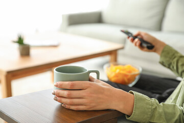 Woman with cup of coffee watching TV on sofa at home