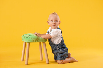 Portrait of cute little baby with stool on color background