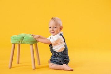 Portrait of cute little baby with stool on color background
