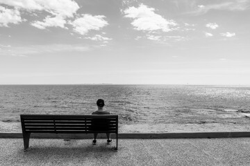 Fotografía callejera en blanco y negro del mar en la costa de Alicante con un banco y una persona sentada de espaldas