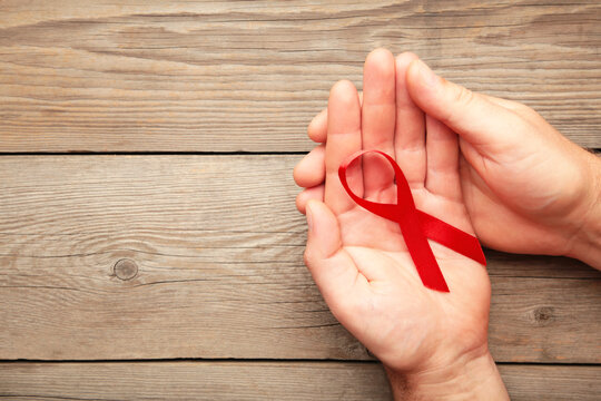 A female hands holding an aids red ribbon on grey