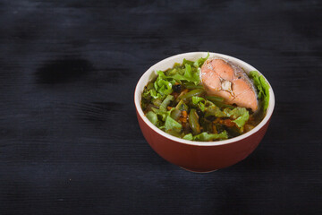 Japanese soup with chum fish, green beans, vegetables, herbs in a clay cup on a black background. Copy spaes.