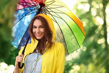 Beautiful young woman with umbrella wearing raincoat in park