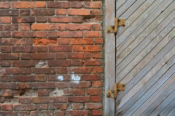 Part of an old wooden door with steel braces and rivets on an antique red brick wall.