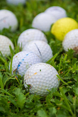 Top view of a group of white golf balls and one yellow, with bokeh, on green grass, vertical