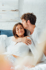 Selective focus of man kissing girlfriend on bed at morning
