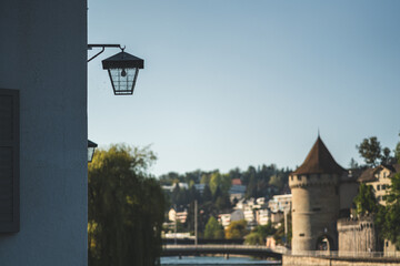 Fototapeta na wymiar A lantern on a house wall by the Reuss river in Lucerne. In the background the powder tower of the Musegg Wall. 