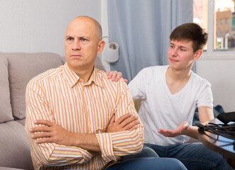 Young teenage guy trying to talk with his offended father