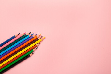 Many different colored pencils on pink background