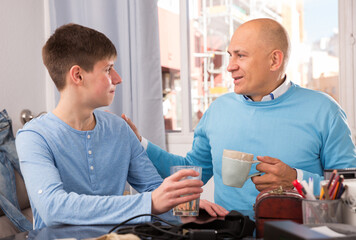 Cheerful teenage guy and his father having conversation together at home