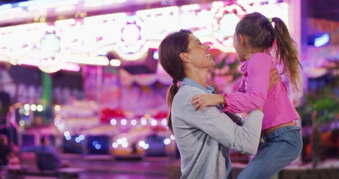 Authentic shot of a happy smiling family is having fun together in amusement park with luna park lights at night.