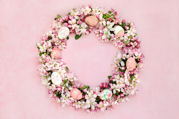 Easter wreath with spring apple blossom flowers & decorated eggs on mottled pink background.  
