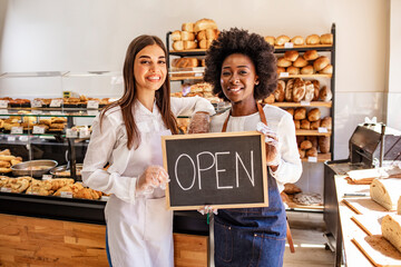 Young business women holding an open sign. Bakery shop female owner showing chalkboard with open sign while opening store. Local business, hospitality, open after lockdown concept.