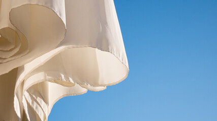 White parasol, blue sky background, wind movement, shadows on white textile