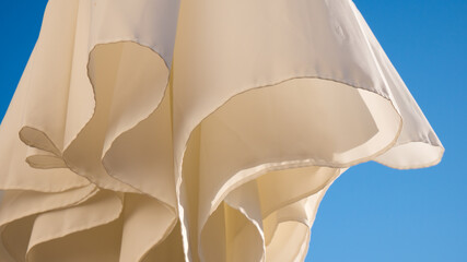 White parasol, blue sky background, wind movement, shadows on white textile