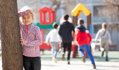 Smiling little girl playing hide and seek and counting while other players hiding, children having fun outdoors on playground