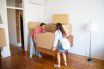 Fototapeta na wymiar Young family couple moving into new apartment, carrying carton boxes and furniture. Full length. Real estate or property buying concept