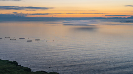 Low clouds over sea during sunrise in Scotland. Fish aquaculture farming round nets in sea
