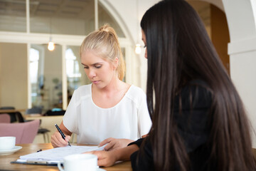 Female agent and customer meeting at co-working for signing agreement. Woman writing in document. Medium shot. Consultation or deal concept
