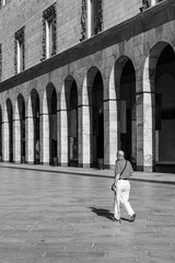 An elderly man with walking stick walks through the streets of the city of Milan