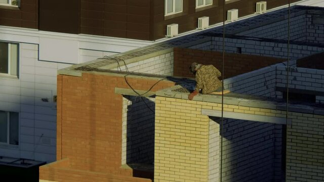 Worker Sits On The Edge Of A Tall Building And Cooks A Metal Structure