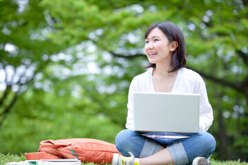 芝生に座りノートＰＣをやる女性