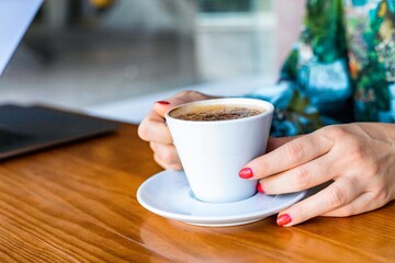 Portrait of a young woman sitting at the cafe and enjoying cup of coffee. The coffee bar is next to the train station of Lisbon, Portugal. Is a place with wooden tables and fresh tasty food.