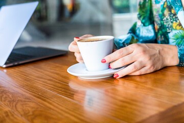 Portrait of a young woman sitting at the cafe and enjoying cup of coffee. The coffee bar is next to the train station of Lisbon, Portugal. Is a place with wooden tables and fresh tasty food.