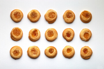 Fifteen handmade cookies with apricot jam arranged in even rows on white background