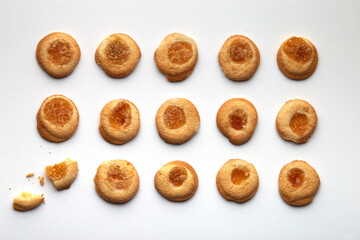 Fifteen handmade cookies with apricot jam arranged in even rows on white background. One in the corner is broken.