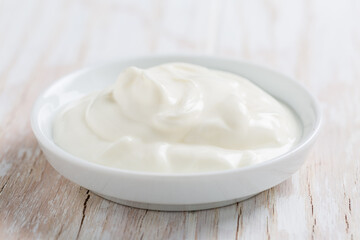 Organic white yogurt or sour cream in bowl on white wooden background