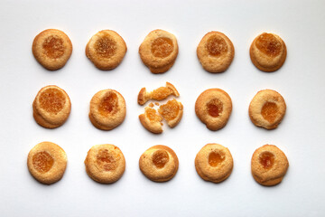 Fifteen handmade cookies with apricot jam arranged in even rows on white background. One in the center is broken.