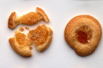 Two handmade cookies with apricot jam arranged in even rows. One is broken. on white background