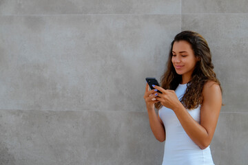 Fototapeta premium Young beautiful woman of Arabic ethnicity wearing tight white dress standing near the grunged concrete textured wall. Close up, copy space, background.