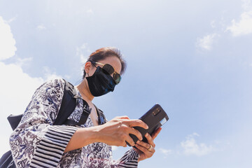 Tourist woman in protective face mask using mobile phone outdoor.